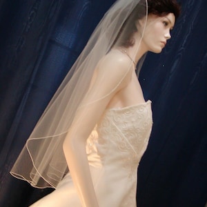 May include: A white wedding dress with a lace bodice and a long, flowing skirt. The dress is paired with a white veil that extends past the bride's shoulders.