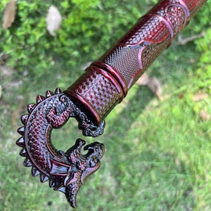 Peut inclure: Une poign&eacute;e de canne m&eacute;tallique rouge fonc&eacute; repr&eacute;sentant une t&ecirc;te de dragon sculpt&eacute;e avec des textures d'&eacute;cailles complexes. Le manche cylindrique attach&eacute; &agrave; la poign&eacute;e pr&eacute;sente un motif en losange r&eacute;p&eacute;titif et une finition brillante.