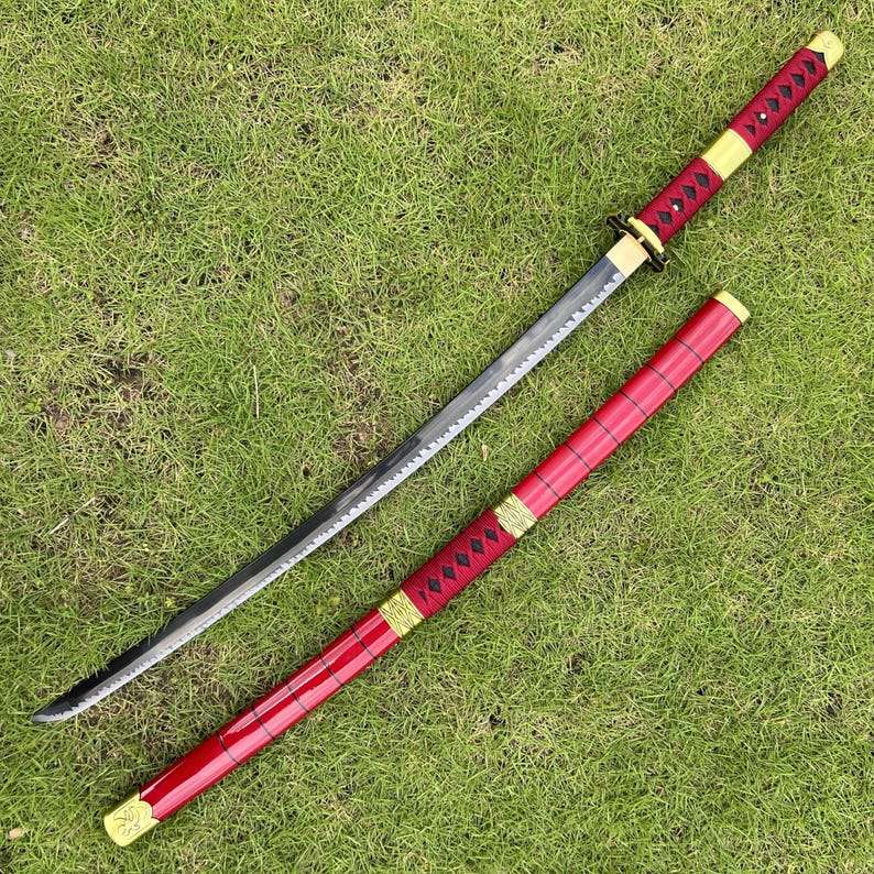 May include: A black and red katana sword with a gold-colored hilt and scabbard. The sword is lying on a green grassy surface.