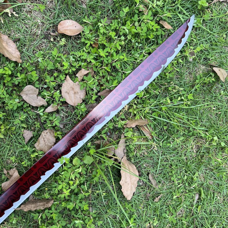 Peut inclure: Une lame d'&eacute;p&eacute;e courbe pr&eacute;sentant une finition rouge profond avec un motif g&eacute;om&eacute;trique sombre r&eacute;p&eacute;titif sur le plat. La lame poss&egrave;de un tranchant argent&eacute; m&eacute;tallique avec une ligne de hamon ondul&eacute;e s&eacute;parant la surface rouge de l'acier.