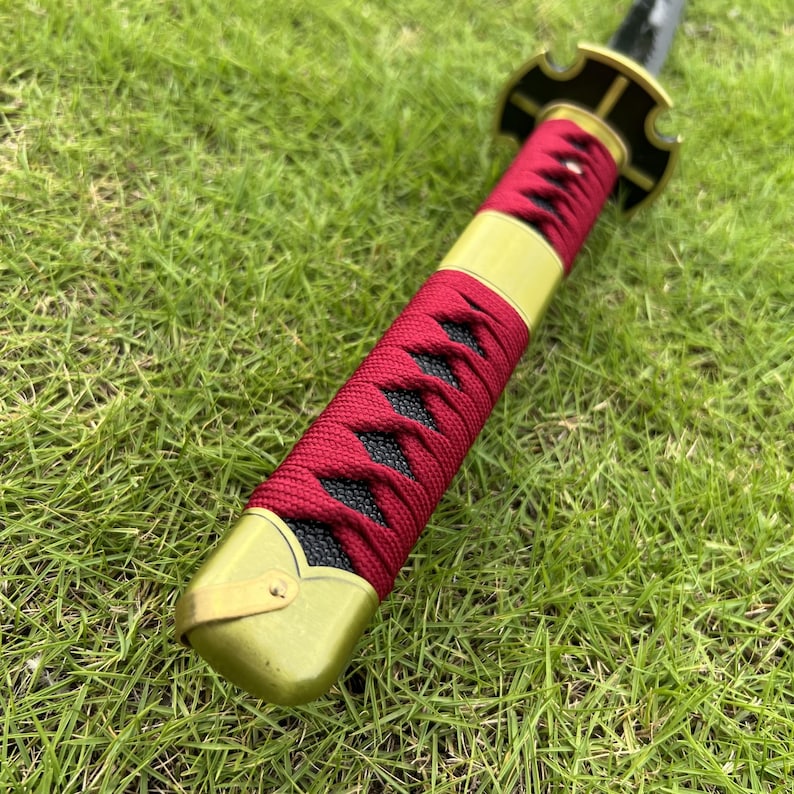 May include: Close-up of a red and black sword scabbard with a gold metal hilt. The scabbard is wrapped in red cord and has a black fabric underneath.