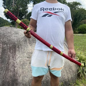 May include: A person holding a red and gold katana sword with a black handle. The sword has a decorative pattern on the blade.