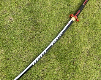Peut inclure: Un katana noir et blanc avec une poignée rouge et blanche. L'épée est posée sur une surface herbeuse verte.