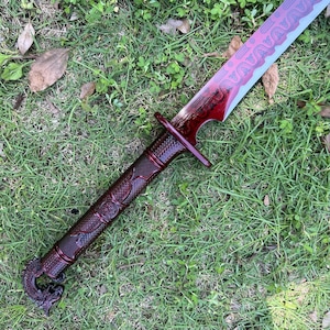 Peut inclure: Une &eacute;p&eacute;e avec une finition m&eacute;tallique rouge fonc&eacute; sur la poign&eacute;e et la lame. La poign&eacute;e pr&eacute;sente une prise textur&eacute;e et un pommeau en forme de dragon. La lame affiche un motif ondul&eacute; rouge fonc&eacute; sur le bord et une finition argent&eacute;e m&eacute;tallique.