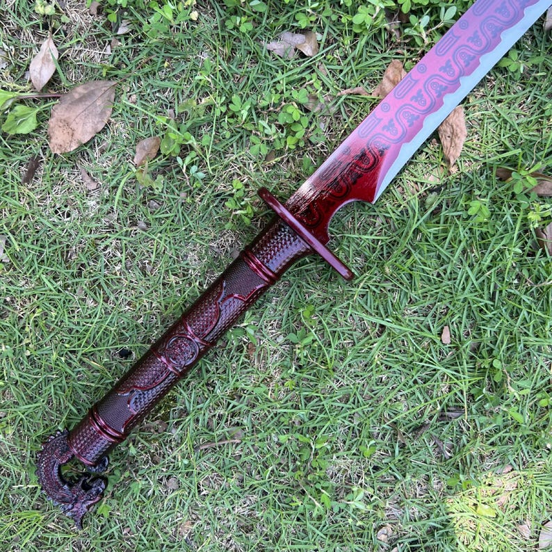 Peut inclure: Une &eacute;p&eacute;e avec une finition m&eacute;tallique rouge fonc&eacute; sur la poign&eacute;e et la lame. La poign&eacute;e pr&eacute;sente une prise textur&eacute;e et un pommeau en forme de dragon. La lame affiche un motif ondul&eacute; rouge fonc&eacute; sur le bord et une finition argent&eacute;e m&eacute;tallique.