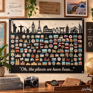 May include: A large black rectangular metal display board featuring a laser-cut skyline silhouette at the top and numerous colorful travel souvenir magnets arranged in rows. The text "Oh, the places we have been..." is printed in white at the bottom.
