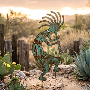 Op de afbeelding: Een turquoise metalen Kokopelli tuinpaal. Het silhouet toont een fluitspeler met uitsparingen van een woestijnlandschap, waaronder cactussen en een zon. Het metaal heeft een verweerde, rustieke uitstraling en de paal staat in een tuin.