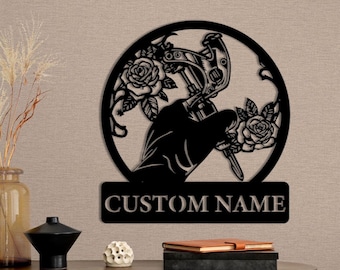 May include: Black metal wall art featuring a tattoo machine with roses and the text "CUSTOM NAME".