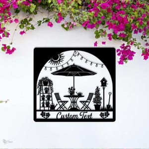 May include: Black metal garden scene with a patio umbrella, table, chairs, and potted plants. The design includes a sun, string lights, and a birdhouse. The words "Custom Text" are at the bottom.