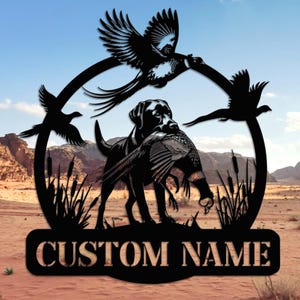 Può includere: Cartello in metallo nero raffigurante un Labrador Retriever con un fagiano, tre uccelli in volo e la scritta "CUSTOM NAME". Il cartello è ambientato su uno sfondo di un paesaggio desertico e cielo blu.