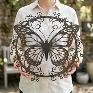 May include: A dark brown metal butterfly wall art. The butterfly is centered within a circular frame with decorative scrollwork. The butterfly's wings are detailed with intricate patterns, and the overall design is suitable for indoor or outdoor decor.