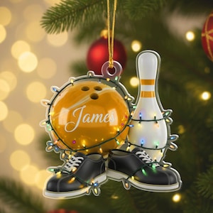 May include: A Christmas ornament featuring a bowling theme. The ornament includes a yellow bowling ball with the name "James", a white bowling pin with orange stripes, and a pair of black bowling shoes. The ornament is decorated with colorful string lights.