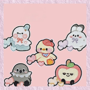 Puede incluir: Parches bordados con personajes de dibujos animados: un fantasma, un patito, un conejito, un pájaro y una manzana. Cada personaje tiene un diseño único y está rodeado de corazones rosas. Los parches están sobre un fondo rosa.