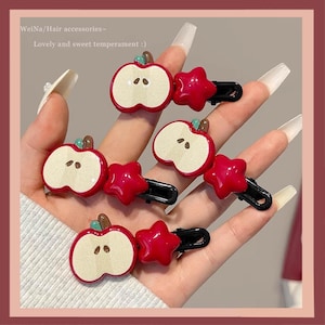 Pode incluir: Acessórios de cabelo com presilhas de cabelo vermelhas em forma de maçã e estrela. Os clipes de maçã têm um interior bege claro com sementes marrons. O texto na imagem diz "WeiNa/Hair accessories~ Lovely and sweet temperament :)".