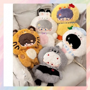May include: A selection of plush toys shaped like animals, such as a tiger, rabbit, duck, and hippo. The toys are predominantly white, yellow, orange, and grey, with embroidered faces and character details. They are displayed on a soft, light-coloured surface.