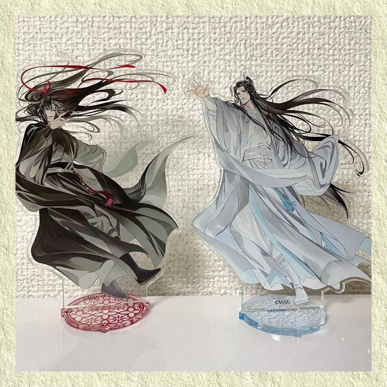 May include: Two acrylic anime character figures. One figure is in black and gray robes with red accents, the other in white and light blue robes. Both figures have long black hair and are on decorative bases.