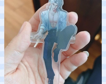 May include: A clear acrylic standee featuring a male anime character with silver hair, wearing a light blue open shirt and dark blue pants. The character is in a seated pose. The standee is held in a hand.