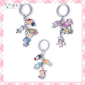 May include: Three silver keychains with cartoon character charms. Each keychain has a large silver ring and a chain holding multiple colorful charms. The charms feature anime-style characters in various poses and outfits. The background is white.