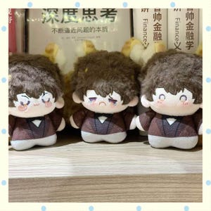May include: Three plush dolls with brown hair and sad facial expressions. They wear brown and white outfits with a bow tie. The dolls are in front of a bookshelf with Chinese text.