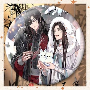 Könnte beinhalten: Ein runder Button mit zwei Anime-Charakteren. Einer trägt ein schwarz-rotes Outfit mit Augenklappe, der andere einen weißen Kapuzenmantel. Sie halten weiße Plüschtiere eines Fuchses und eines Bären.