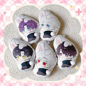 May include: A collection of five plush keychains featuring anime-style characters with bunny ears. Each keychain has a different hair color, including purple, white, black, and red. The characters are wearing black outfits and have white bunny tails.