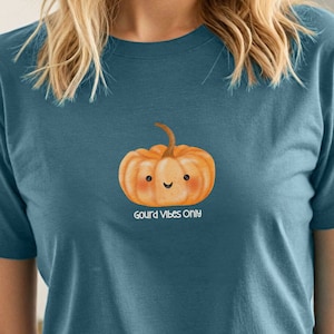 Op de afbeelding: Een tealblauw t-shirt met een cartoonpompoen met een glimlachend gezicht en de tekst "Gourd Vibes Only".
