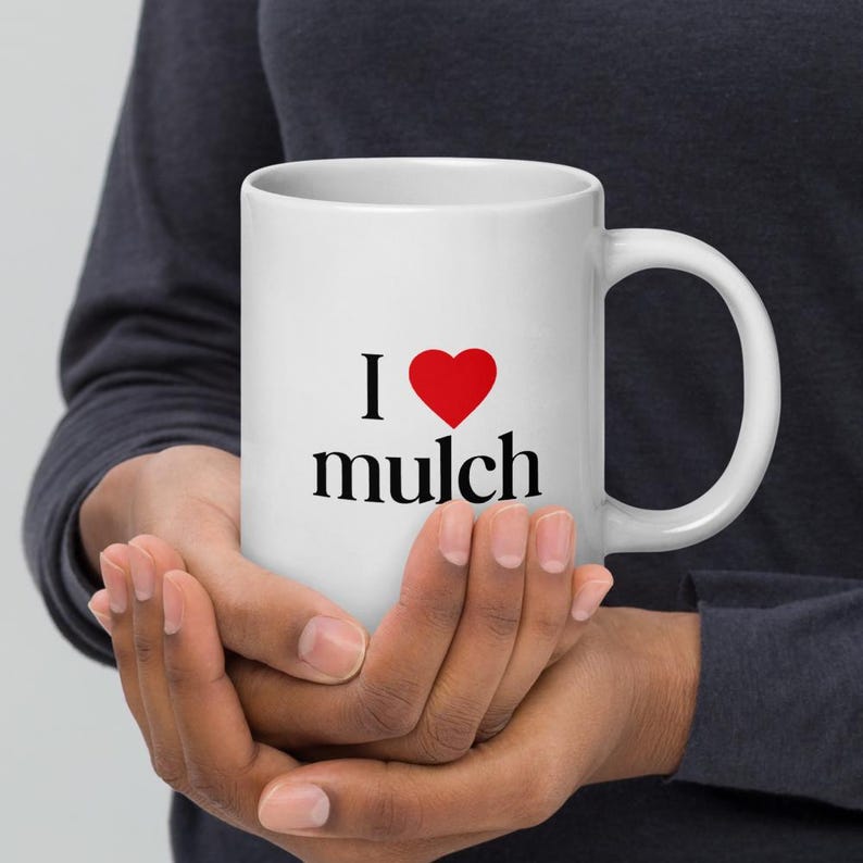 K&ouml;nnte beinhalten: Eine wei&szlig;e Keramik-Kaffeetasse mit einem roten Herzen und dem Text "Ich liebe Mulch" darauf.