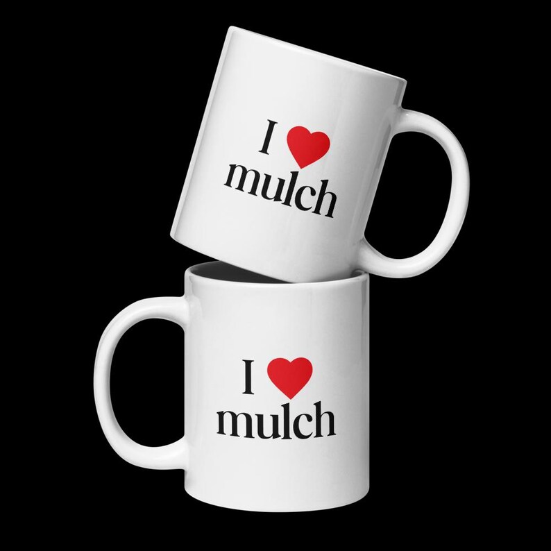 K&ouml;nnte beinhalten: Zwei wei&szlig;e Keramikbecher, die &uuml;bereinander gestapelt sind. Beide Becher haben ein rotes Herz und den Text "Ich liebe Mulch" aufgedruckt.