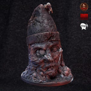 May include: A detailed, dark sculpture of a decaying face with a pointed head. The sculpture is a mix of dark reds and browns, with a small figure on top and flies on the face. The base is round and the overall theme is horror.