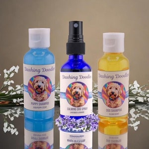 May include: Three bottles of dog shampoo and spray featuring a doodle dog on each label. The bottles are blue, yellow, and clear. The labels read "Dashing Doodles" and list the scents: "Puppy Shampoo", "Calming Dog Spray", and "Dog Shampoo".