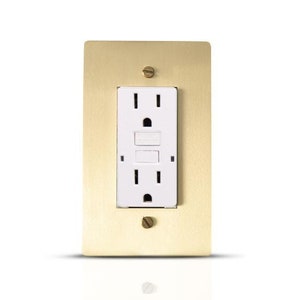 May include: A brass electrical outlet cover with a white standard outlet inside. The outlet cover has a brushed finish and is mounted on a white wall.