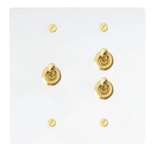 Op de afbeelding: Een witte rechthoekige lichtschakelaarplaat met twee gouden schakelaars. Elke schakelaar heeft een ronde knop en een gouden rand. De plaat heeft vier kleine gouden schroeven.
