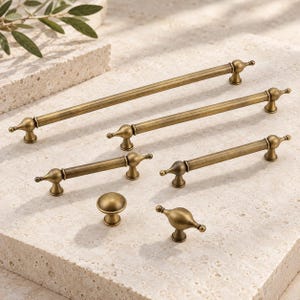 May include: A collection of six antique brass cabinet hardware pieces, including four elongated bar pulls with rounded finials and two smaller knobs, one circular and one spindle-shaped, all featuring a smooth, metallic finish.