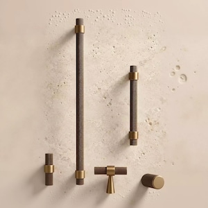 May include: A collection of five cabinet hardware pieces including two long cylindrical pulls, one shorter cylindrical pull, one T-shaped pull, and one round knob. Each piece features a dark brown knurled texture with smooth brass-toned metal accents.
