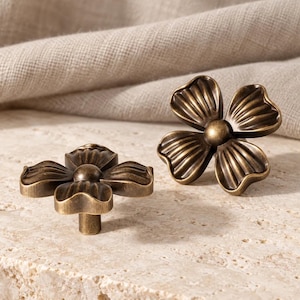 Peut inclure: Deux boutons de placard en laiton antique en forme de fleurs à quatre pétales. Chaque bouton présente un bouton central circulaire avec des pétales rainurés rayonnants dotés d'une finition sombre et patinée. Base cylindrique incluse.