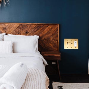 May include: A white bed with a wooden headboard and a white blanket. The bed is in a room with a dark blue wall and a gold light switch.