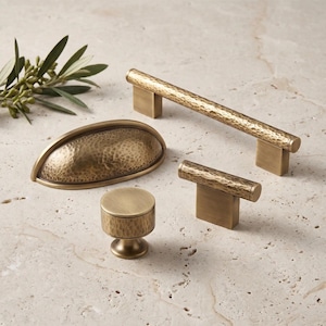 May include: A collection of four brass cabinet hardware pieces featuring a hammered texture. The set includes one long bar pull, one cup pull, one T-shaped knob, and one round knob, all finished in a muted, antique-style metallic gold tone.