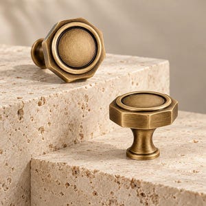 Può includere: Due pomelli per armadietti in ottone con forma ottagonale e centro circolare. Ogni pomello presenta una finitura metallica spazzolata con un anello scuro che accentua il cerchio interno. La ferramenta ha una base svasata.