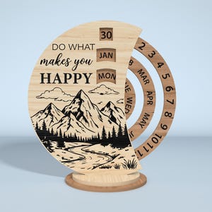 Puede incluir: Un calendario perpetuo de madera con un dise&ntilde;o de monta&ntilde;a y r&iacute;o. El calendario muestra el texto "DO WHAT makes you HAPPY" e incluye anillos giratorios para el mes y el d&iacute;a. La fecha es el 30 de enero, lunes.