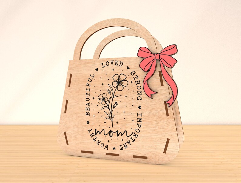 May include: Wooden cutout of a handbag with a pink bow. The handbag has the words "mom", "loved", "beautiful", "worthy", "important", and "strong" engraved on it.