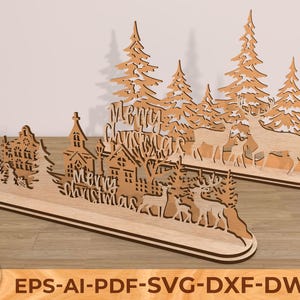 Peut inclure: Deux décorations de Noël en bois. Chacune présente une scène de forêt avec des cerfs, des arbres et des bâtiments. Les mots "Merry Christmas" sont découpés au centre. Les décorations sont en bois brun clair.