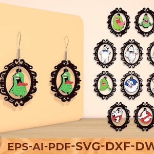Op de afbeelding: Een paar oorbellen met een groen stripfiguur in een bruin frame, gepresenteerd op een beige oppervlak. Extra oorbellen met verschillende stripfiguren zijn ook afgebeeld. De oorbellen zijn ontworpen met een vintage frame stijl.