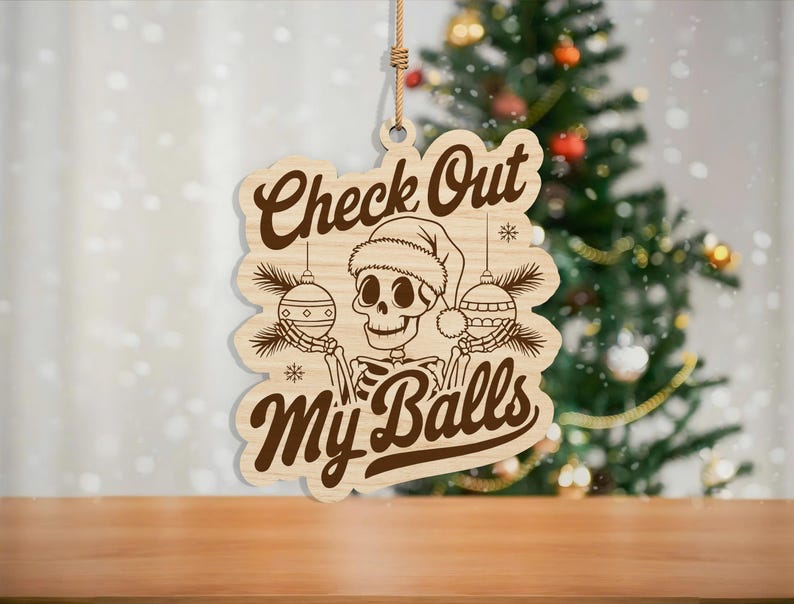 May include: Wooden Christmas ornament with a skeleton wearing a Santa hat and holding ornaments. The ornament has the text "Check Out My Balls" in a brown, vintage font. A rope is attached for hanging.