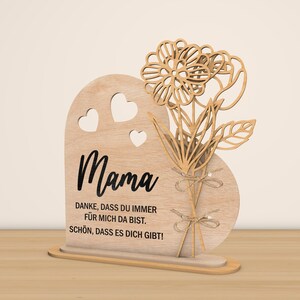 May include: Wooden heart-shaped sign with a cutout of flowers and the word "Mama" in black lettering. The sign also includes the text "Danke, dass du immer fur mich da bist. Schon, dass es dich gibt!"