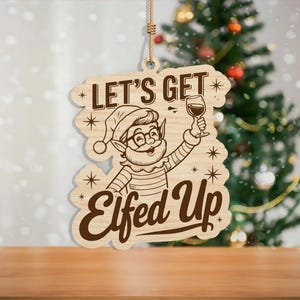 May include: Wooden Christmas ornament with the phrase "Let's Get Elfed Up" and a cartoon elf holding a wine glass. The ornament is light brown with dark brown text and design elements. A festive holiday decoration.