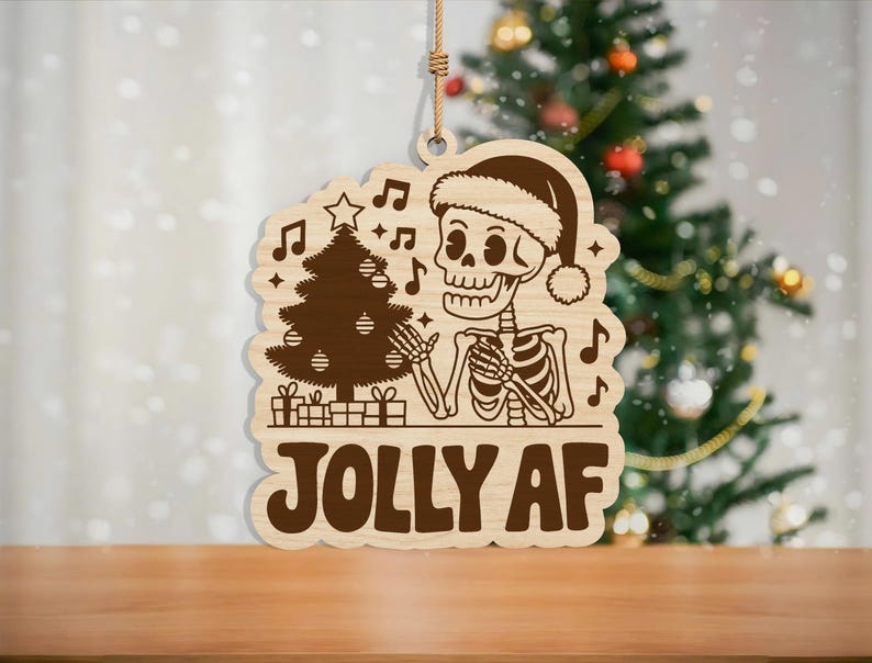 May include: Wooden Christmas ornament featuring a skeleton wearing a Santa hat, with a Christmas tree and musical notes. The text "JOLLY AF" is displayed in bold letters. The ornament is hanging by a natural twine.