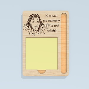 May include: Wooden memo board with a pop art style illustration of a woman and the text "Because my memory is not reliable." The board has a yellow sticky note pad and a pen holder.