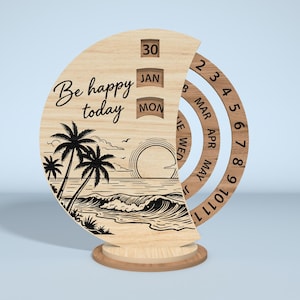 Puede incluir: Calendario perpetuo de madera con una escena de playa y la frase "Be happy today". El calendario muestra la fecha, el mes y el d&iacute;a. El dise&ntilde;o incluye palmeras, olas y un sol poniente. El calendario es de madera clara.