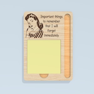 May include: Wooden memo board with a retro illustration of a woman and the text "Important things to remember that I will forget immediately." The board has a yellow sticky note pad and a slot for a pen.
