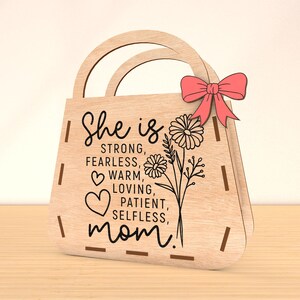 May include: Wooden handbag-shaped sign with the text "She is strong, fearless, warm, loving, patient, selfless, mom!" and a floral design.